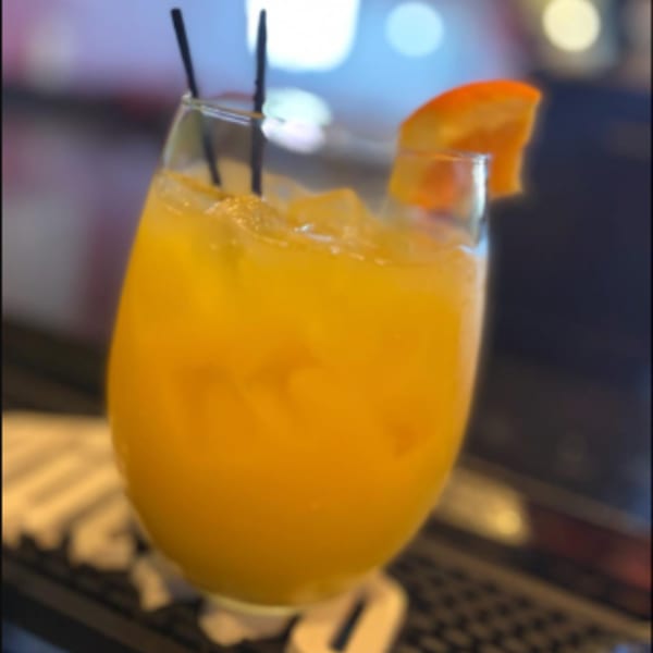 Orange cocktail with ice, two black straws, and an orange slice garnish at J.R. Crickets.