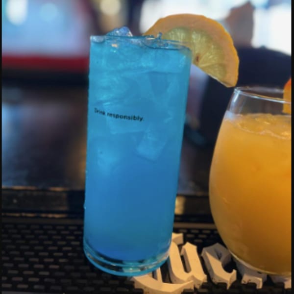 A blue cocktail with a lemon slice and an orange drink on a bar mat.