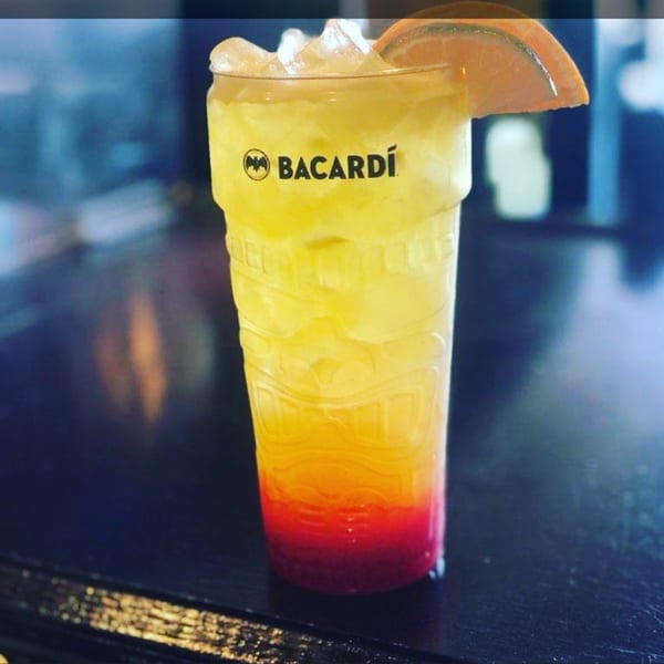 A colorful Bacardi cocktail with ice and an orange slice on a dark surface.
