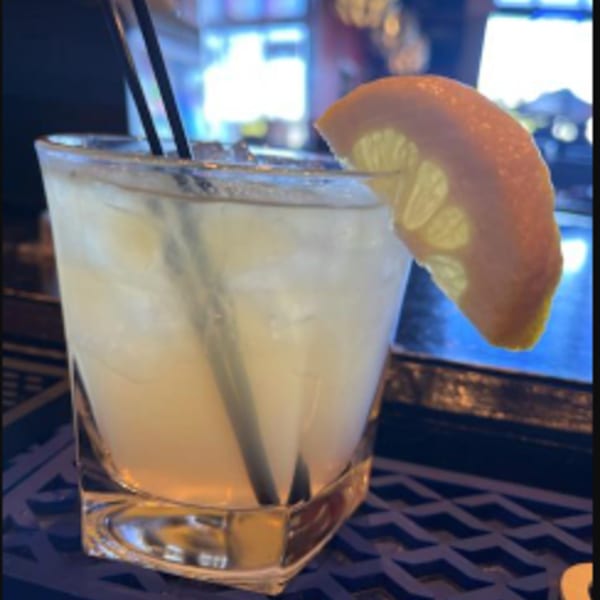 A J.R. Crickets cocktail with ice, two straws, and a lemon slice on a dark patterned surface.