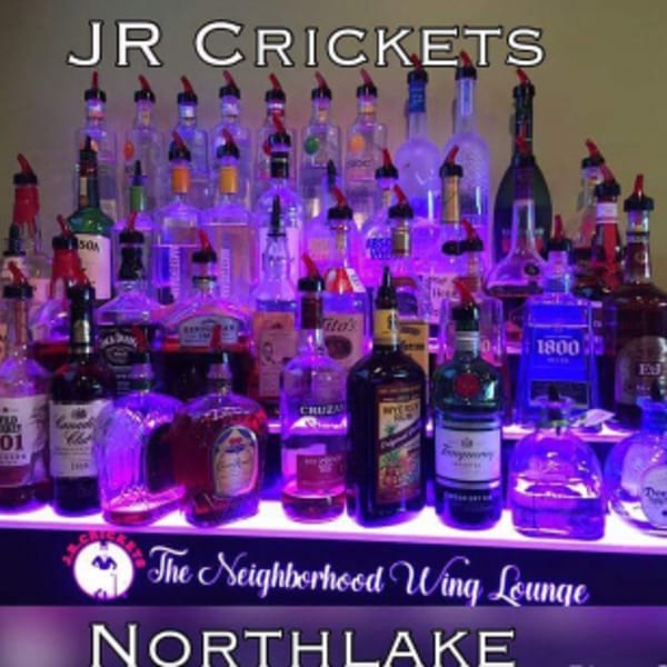 A bar display at J.R. Crickets with numerous liquor bottles illuminated by purple light.